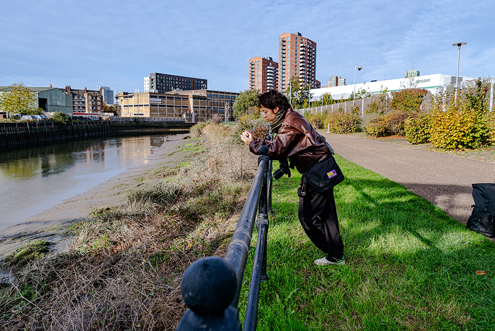 Female figure, metal railing, green grass and the Riverflow, Nikon 24mm